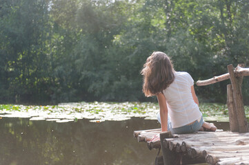 Girl sits on a bridge and looks at the lake. Vacation at the lake.