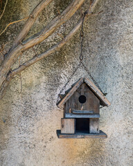 Small and cute traditional handmade wooden birdhouse hanging outdoors on chain against garden wall