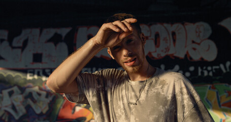 Handsome man relaxing after training at skate park with graffiti wall. 