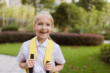 Schoolgirl back to school after summer vacations. Pupil in uniform smiling early morning outdoor.