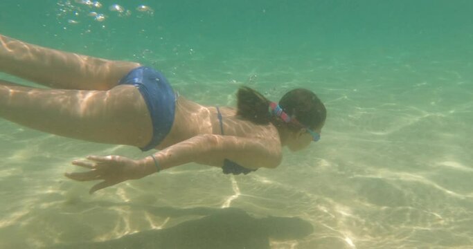 Child girl swimming underwater with swim goggles. Dives and swimming in the sea. Have fun on summer vacation. 4K slow motion.