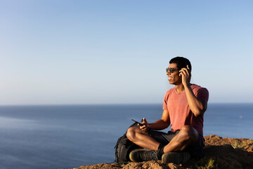 Young man sitting on the stone listening the music. Tourist man on the top of the mountain