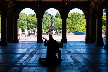 Musician playing guitar inside a building against the fountain in the central park, New York