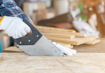 Close up carpenter cuts a wood plank with a hand saw.