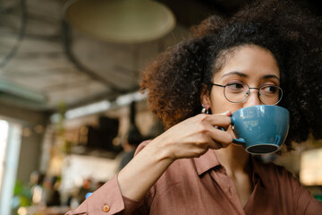 Young african american woman using laptop and drinking coffee in cafe