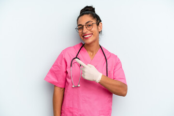 hispanic  woman smiling cheerfully, feeling happy and pointing to the side. nurse concept - obrazy, fototapety, plakaty
