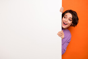 Photo of excited funky girl peeking look interested empty space blank promo isolated on orange...