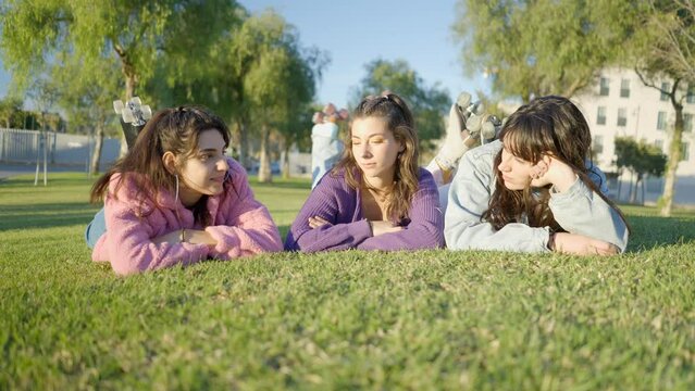 Girls with rollerskates lie on grass in sunlight and chat, ground view