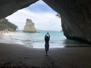 Foto op Aluminium Beautiful view of a female meditating in the Cathedral Cove by the sunny sea water in New Zealand © Lucia Wei/Wirestock Creators