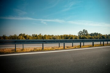 Beautiful shot of a highway guardrail on the side of a road with trees in the background
