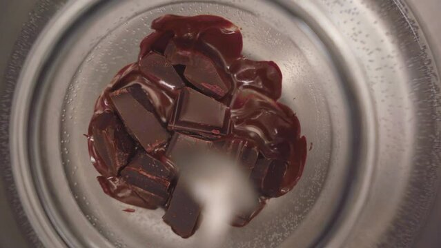 Close up view of a person mixing chocolate from a bowl in a bain marie. The water is boiling and the chocolate is half molten.