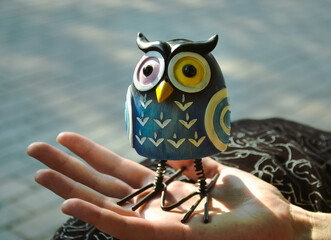 A toy of a surprised blue owl with multi-colored eyes close-up stands on the palm of a female hand...