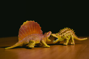 Two figures of aggressive growling dinosaurs stand opposite each other on a brown table against a...