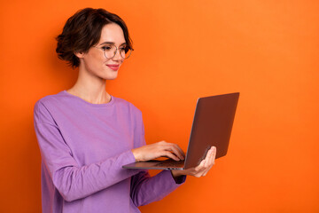 Portrait of smart positive lady hold use wireless netbook write email isolated on orange color background
