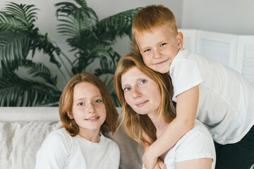 A woman at home sits on the couch with her children. 