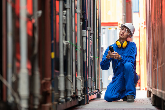 Dock worker man in safety vest holding barcode scanner and looking at container to check defect in shipping yard. Import and export product. Manufacturing transportation and global business concept