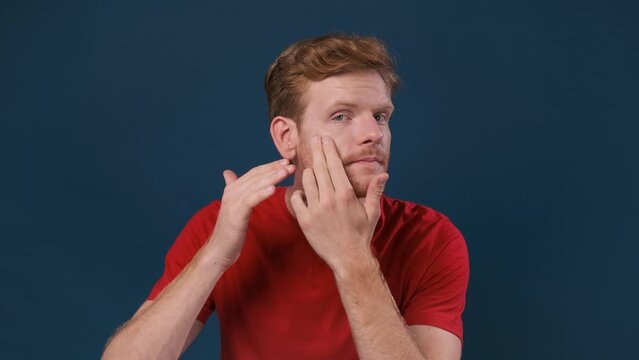 Young man examining his skin problems looking at camera over dark blue background