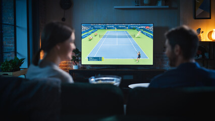 Authentic Couple Spending Time at Home, Sitting on a Couch and Watching Tennis Championship on Flat Screen Television Set. Man and Woman Enjoying Live Broadcast of Sports Finals.