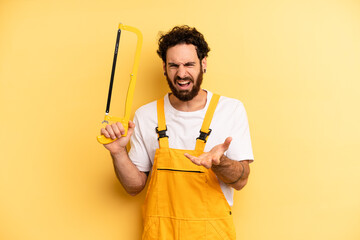 young man looking angry, annoyed and frustrated. handyman with a saw