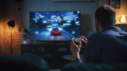 Young Man Spending Time at Home, Sitting on a Couch in Stylish Loft Apartment and Playing Arcade...