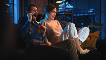 Portrait of Beautiful Couple Spending Time at Home, Sitting on a Couch, Watching Scary TV Show in...