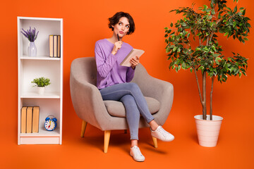 Full body photo of minded pensive person sitting chair pen touch chin isolated on orange color background