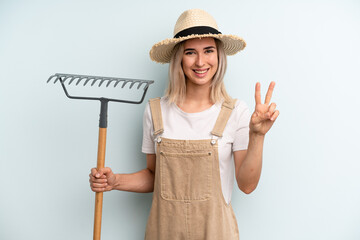 blonde woman smiling and looking friendly, showing number two. farmer and rake cocnept