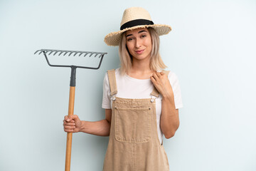 blonde woman looking arrogant, successful, positive and proud. farmer and rake cocnept - obrazy, fototapety, plakaty