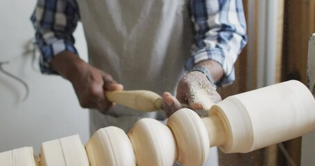 African american male carpenter wearing protective helmet turning wood on a lathe at carpentry shop