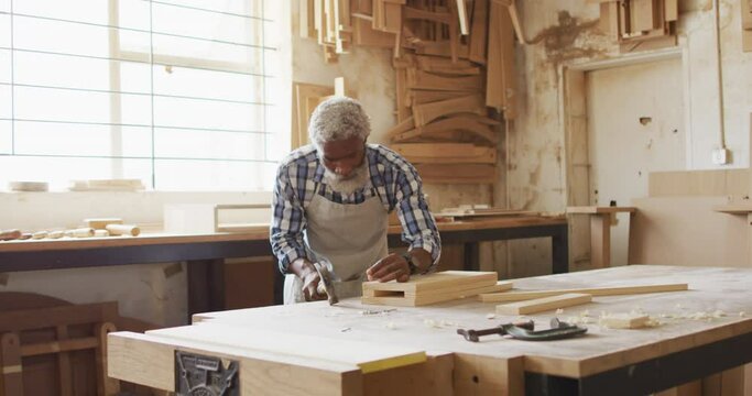 African american male carpenter hammering nails into the wood at a carpentry shop