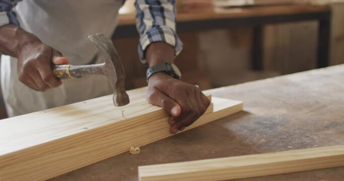 Mid section of african american male carpenter hammering nails into the wood at a carpentry shop