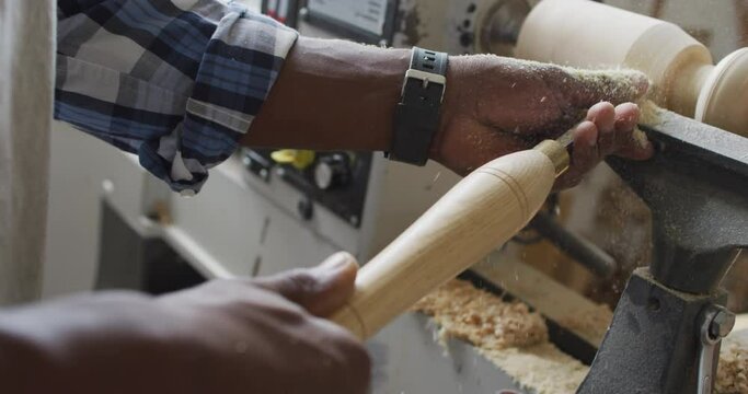 Close up of african american male carpenter hand's turning wood on a lathe at carpentry shop