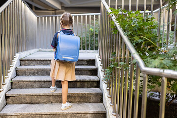 Schoolgirl back to school after summer vacations. Child in uniform standing early morning outdoor. Lifestyle portrait of Little caucasian girl with blonde hair six-seven years old from elementary