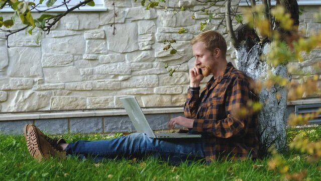 Man Talking On The Phone And Working On A Laptop While Sitting In The Garden