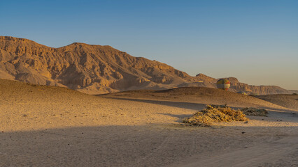 Balloons rise over the desert from the gorge. Shadows on the sand hills. A picturesque mountain range against a clear blue sky. Egypt. Luxor