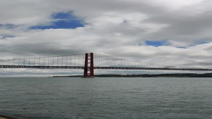 Vertical shot 25th of April Bridge under a blue cloudy sky  in Lisbon, Portugal