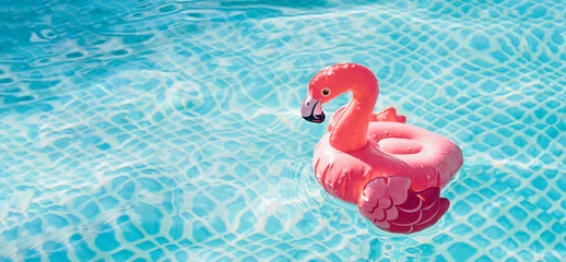 Gardinen Small inflatable flamingo on blue water background, summer concept banner © Irina