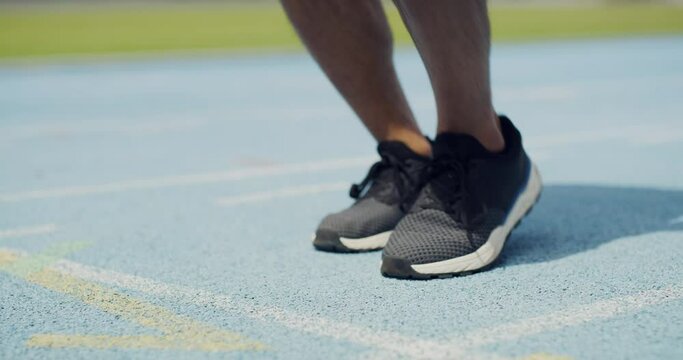 Closeup of athlete tying shoe laces and jumping in place before running and exercise. Feet of runner warming up and getting ready to run in a race. Endurance and fitness training for competition
