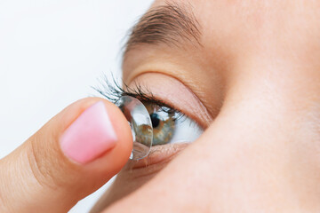 Close up of a young woman applying eye lens with her hand isolated on a white background. The girl...