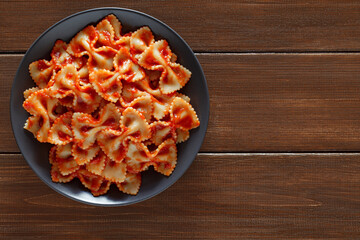 Farfalle, cooked pasta with tomato sauce, on wooden brown plank table top background, top view,...