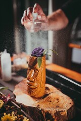 Vertical shot of a bartender spraying water on a cocktail in a wooden tiki cup.