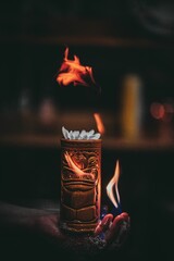 Vertical shot of a burning cocktail in a tiki cup on a bratender's hand.