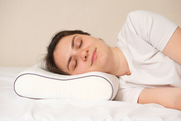 A woman sleeps on an orthopedic pillow made of memory foam, lying on a bed. The correct pillow for a comfortable healthy sleep.