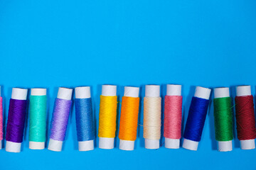 A set of multi-colored threads for sewing with an empty space for text on a blue background, top view. Tailoring and needlework equipment, tailor banner.