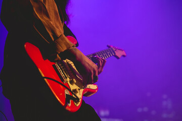 Closeup of young latino guitar player with shirt and red guitar playing live in a concert under...