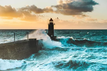 Deurstickers Large waves crash against the stone tower of the lighthouse at high tide at sunset © Alexis21/Wirestock Creators
