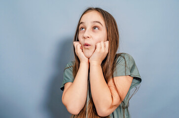 Playful little girl waiting for a gift. She is surprised, holding her hands under her chin. Gray background.