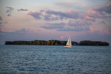 Beautiful shot of the blue water and white sailboat passing by with a pink sunset in the background