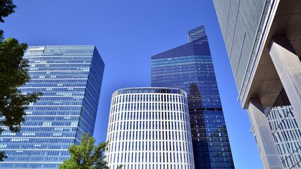 Obraz premium Bottom view of modern skyscraper in business district against blue sky. Looking up at business buildings in downtown. Rising sun on the horizon.