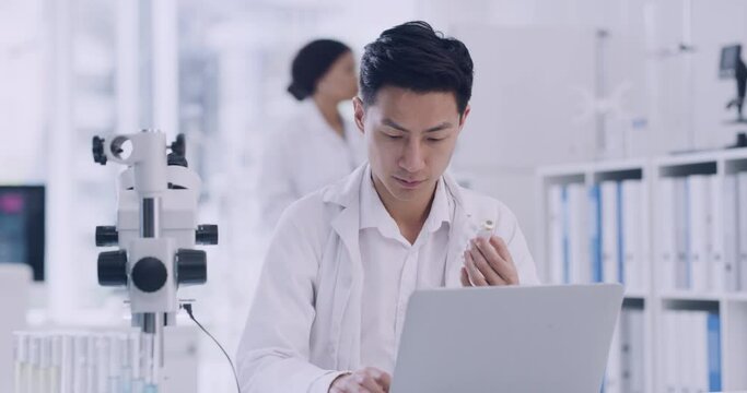 Scientist using a laptop while analyzing test tubes of samples in a lab. Male pathologist doing forensic research while assessing data online. Clinical researcher recording results from experiments